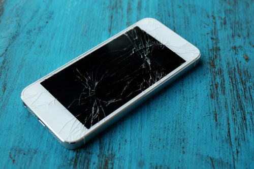 Modern mobile phone with broken screen on wooden background
